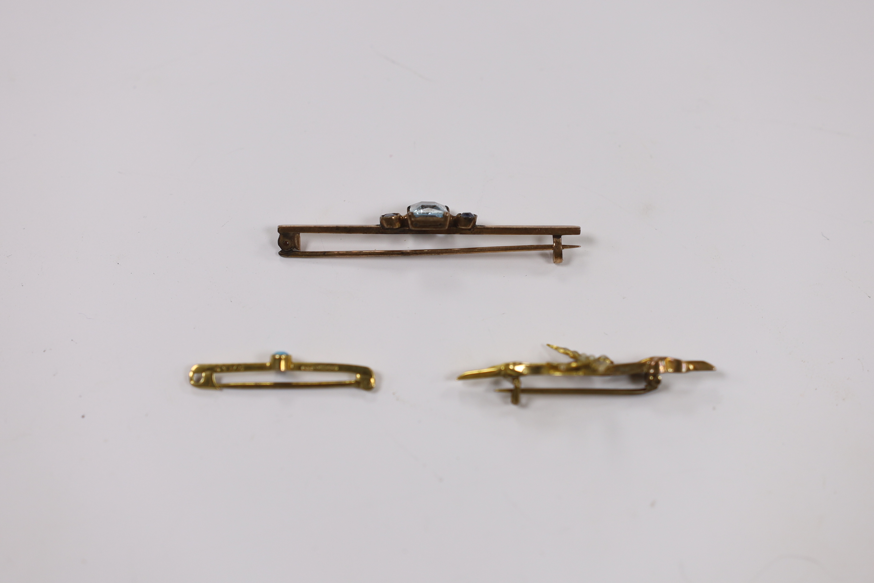 An Edwardian 9ct gold and seed pearl set swallow bar brooch, 43mm, a 9ct gold and turquoise set tie pin and a yellow metal, single stone aquamarine and two stone sapphire set bar brooch. Fair condition.